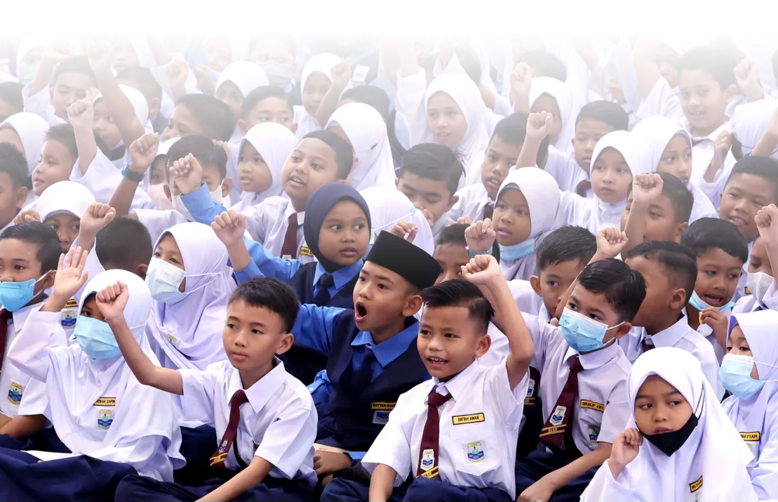 Malaysian schoolchildren in uniform raising their hands at an assembly